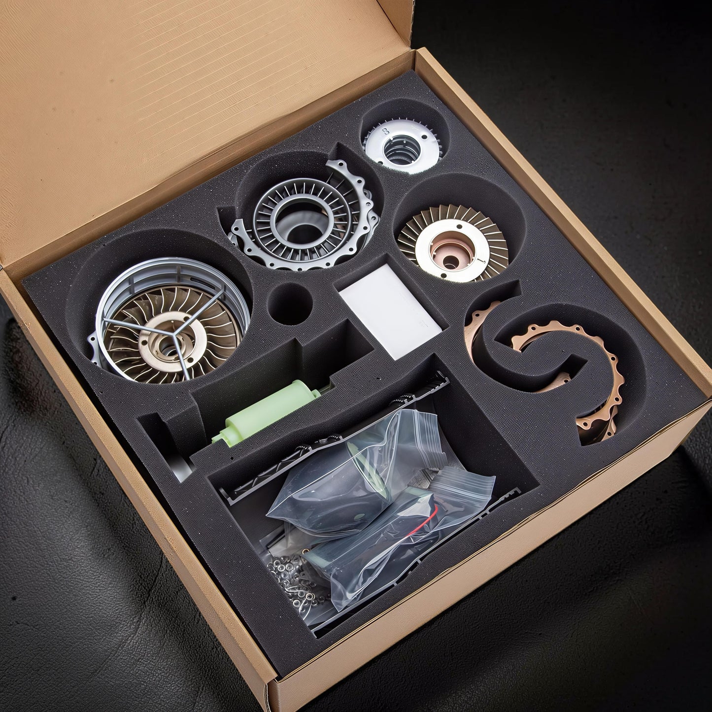 The Curious Mind WS-15 Fighter Turbofan DIY Kit with metal and plastic components neatly organized in a cardboard box with foam inserts.